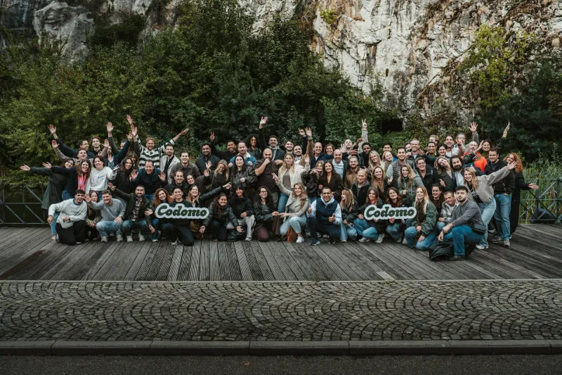 Photo de groupe des équipes de Codomo, bras levés, pendant leur team building à Durbuy