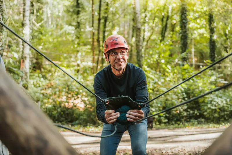 A participant in a helmet holding the ropes of a team game in the forest, during a team building in Durbuy