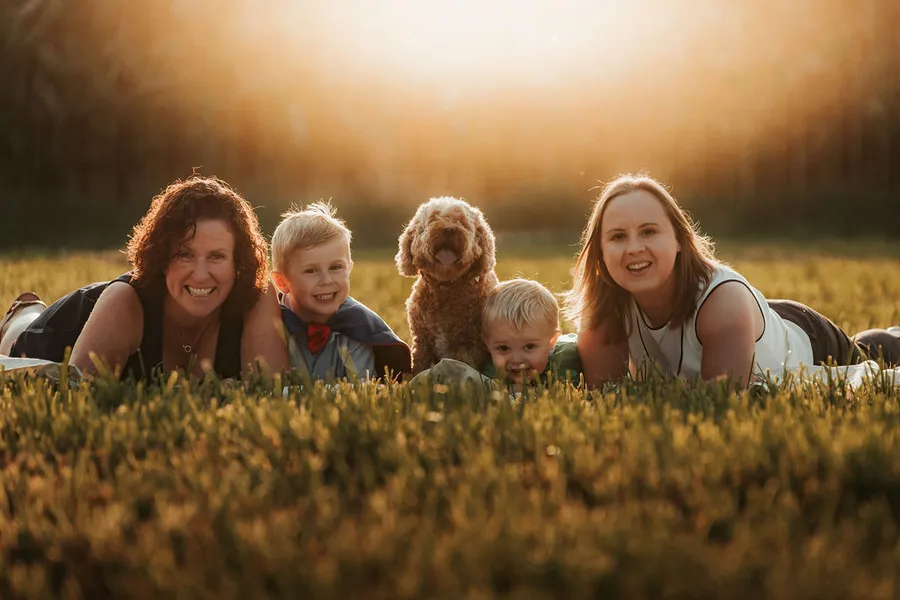 Famille allongée dans l'herbe avec les enfants et le chien, au coucher du soleil